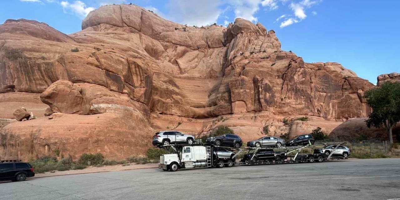 A loaded JDS car carrier parked below red rock cliffs on a western interstate run