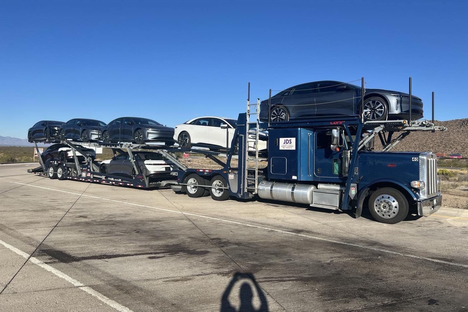 A loaded JDS carrier carrying new electric sedans, stopped on a desert interstate shoulder